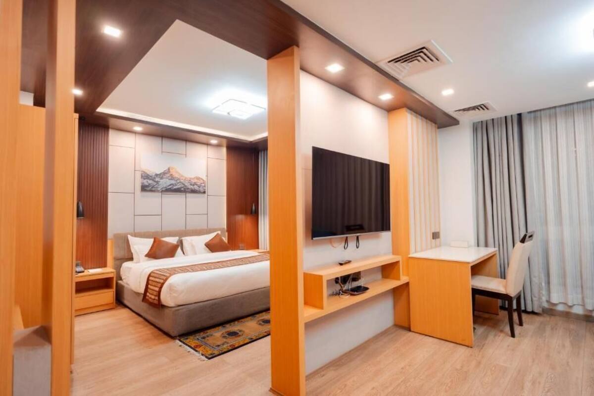A modern hotel room with a bed, TV, desk, and storage units.