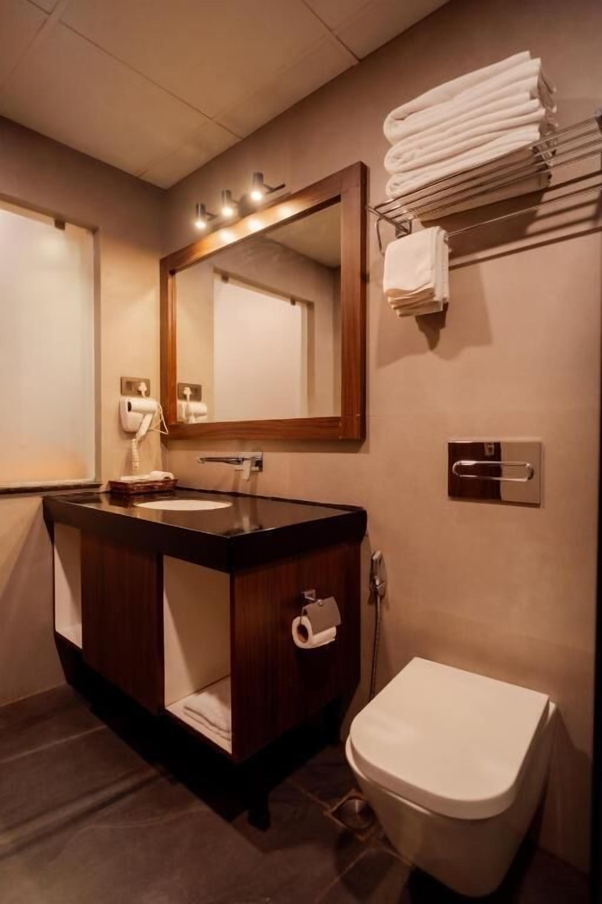 Un baño moderno con tocador de madera oscura, un espejo grande y un inodoro blanco.