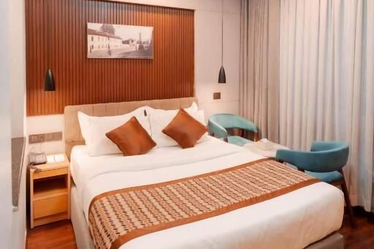A modern hotel room with a large bed, wooden panel wall, and a ceiling light fixture.
