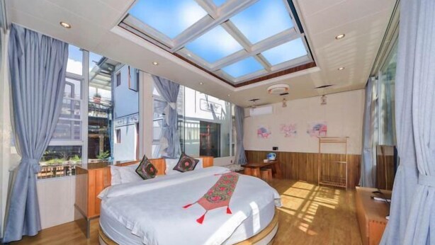 A modern bedroom with a skylight, a round bed, and a view of the city.