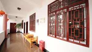 A hallway with traditional Chinese window designs, a wooden bench, and a potted plant.