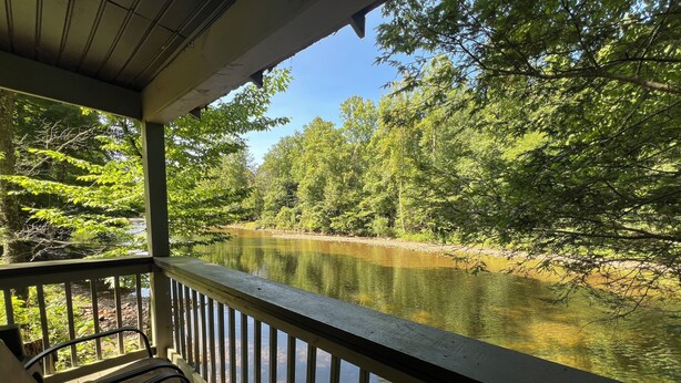 A covered outdoor seating area with a view of a river and surrounding trees. - Charming riverfront home with beautiful views, hot tub and game room. Fishing! (Elkins)
