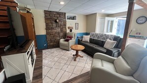 A cozy living area with a stone accent wall, a sofa, a chair, and a small round table. - Charming riverfront home with beautiful views, hot tub and game room. Fishing! (Elkins)