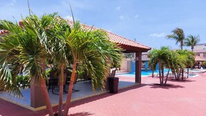 Ein Poolbereich mit Palmen, einer überdachten Sitzgelegenheit und blauem Himmel.