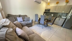 Ein modernes Wohnzimmer mit einer Eckcouch, einem Esstisch mit Stühlen und einer Küchenzeile inklusive Mikrowelle und Kühlschrank.