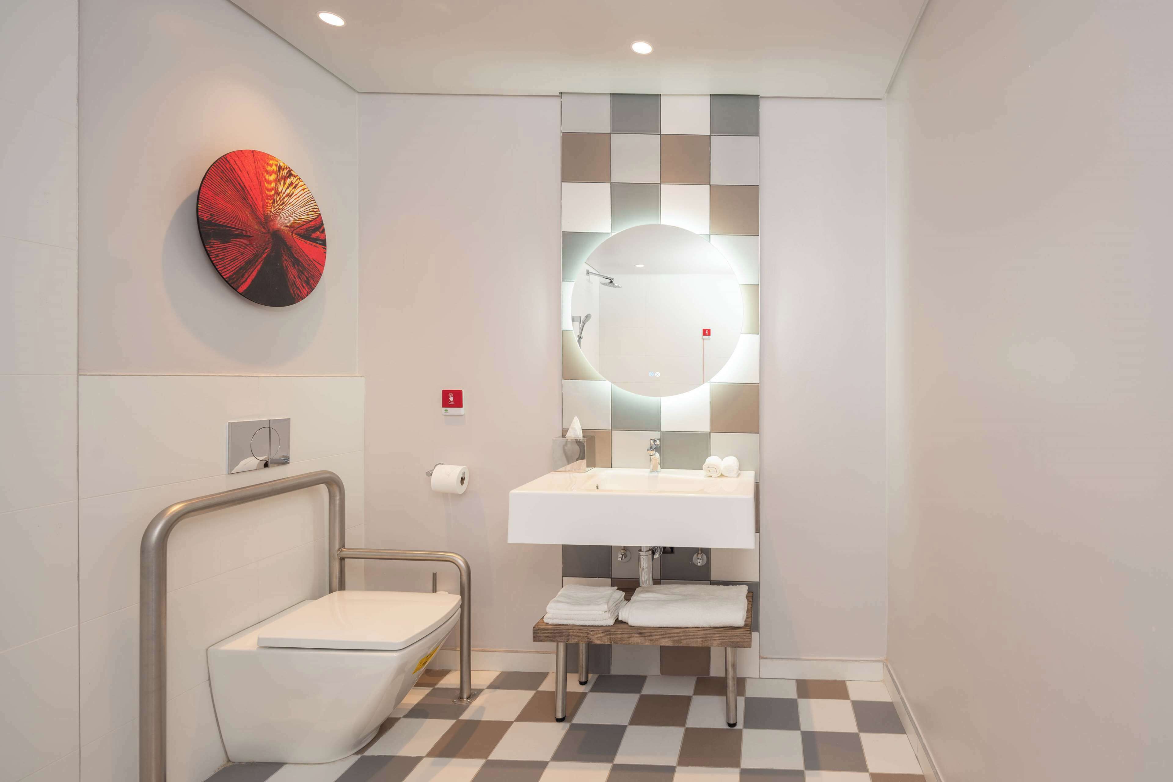 Un baño moderno con un lavamanos blanco, un espejo redondo y un inodoro.