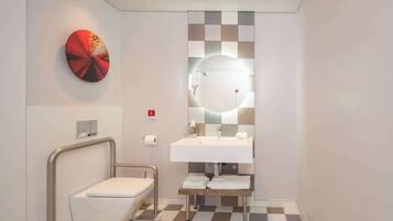 Un baño moderno con un lavamanos blanco, un espejo redondo y un inodoro.
