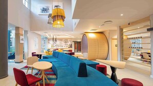 Ein moderner Lounge-Bereich mit blauem Sofa, roten Sesseln und einem Holzfass-Element.