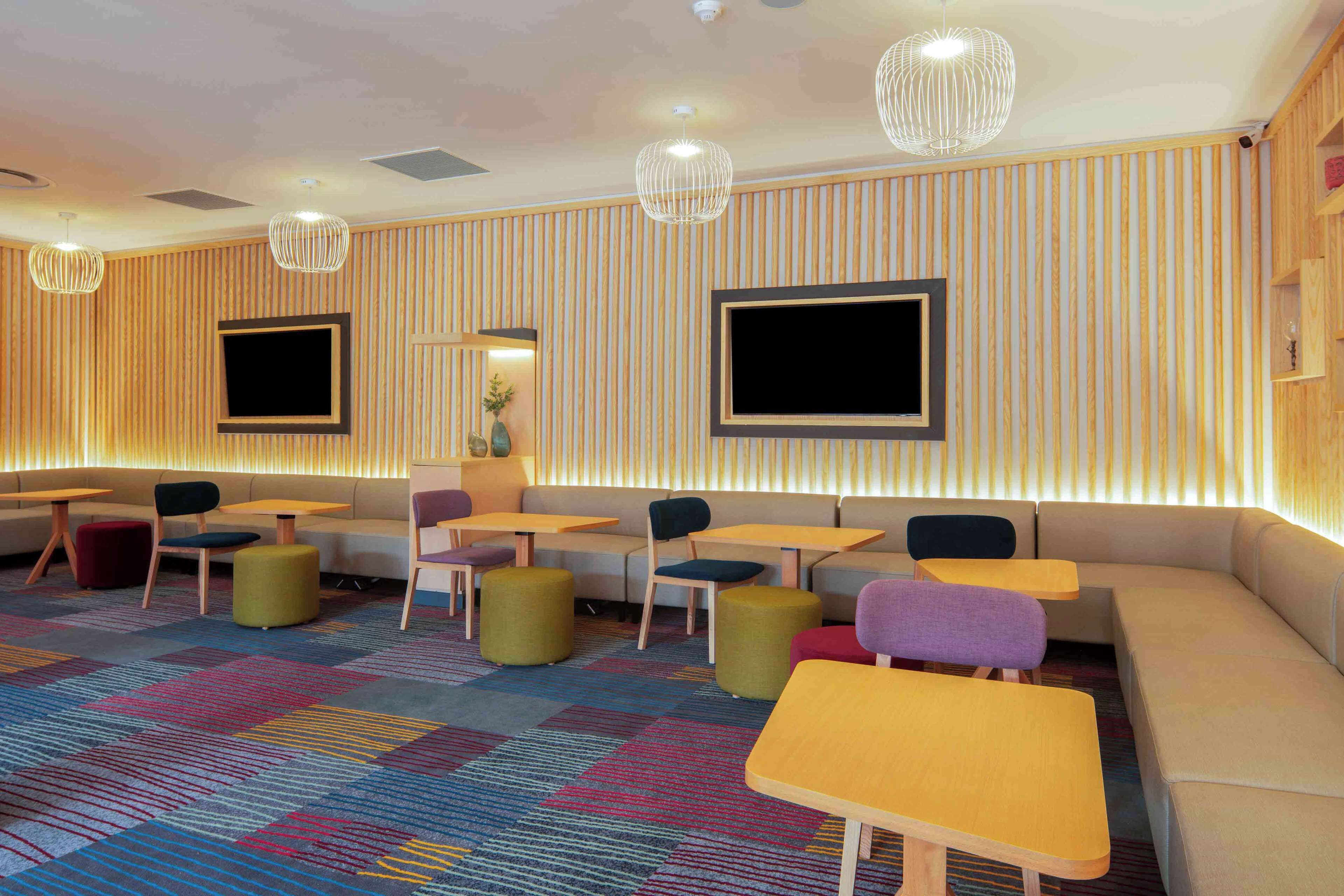 A modern lounge area with seating arrangements, tables, and a patterned carpet.