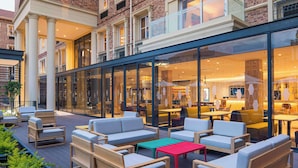 Ein moderner Außenbereich mit Sofas und Tischen, ein Restaurant mit Glasfassade und eine Backsteingrundmauer.