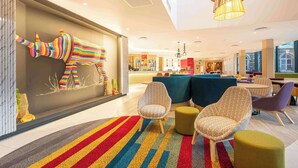 Eine moderne Hotelhalle mit Streifenoptik-Teppich, gemusterten Sesseln und einer farbenfrohen Wanddekoration.