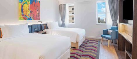 Habitación de hotel con dos camas, televisión, escritorio, silla, alfombra colorida y un cuadro en la pared.