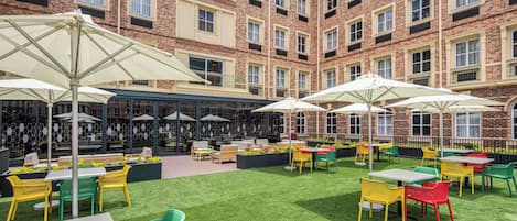 A courtyard with outdoor seating, a bar, and a brick building in the background.