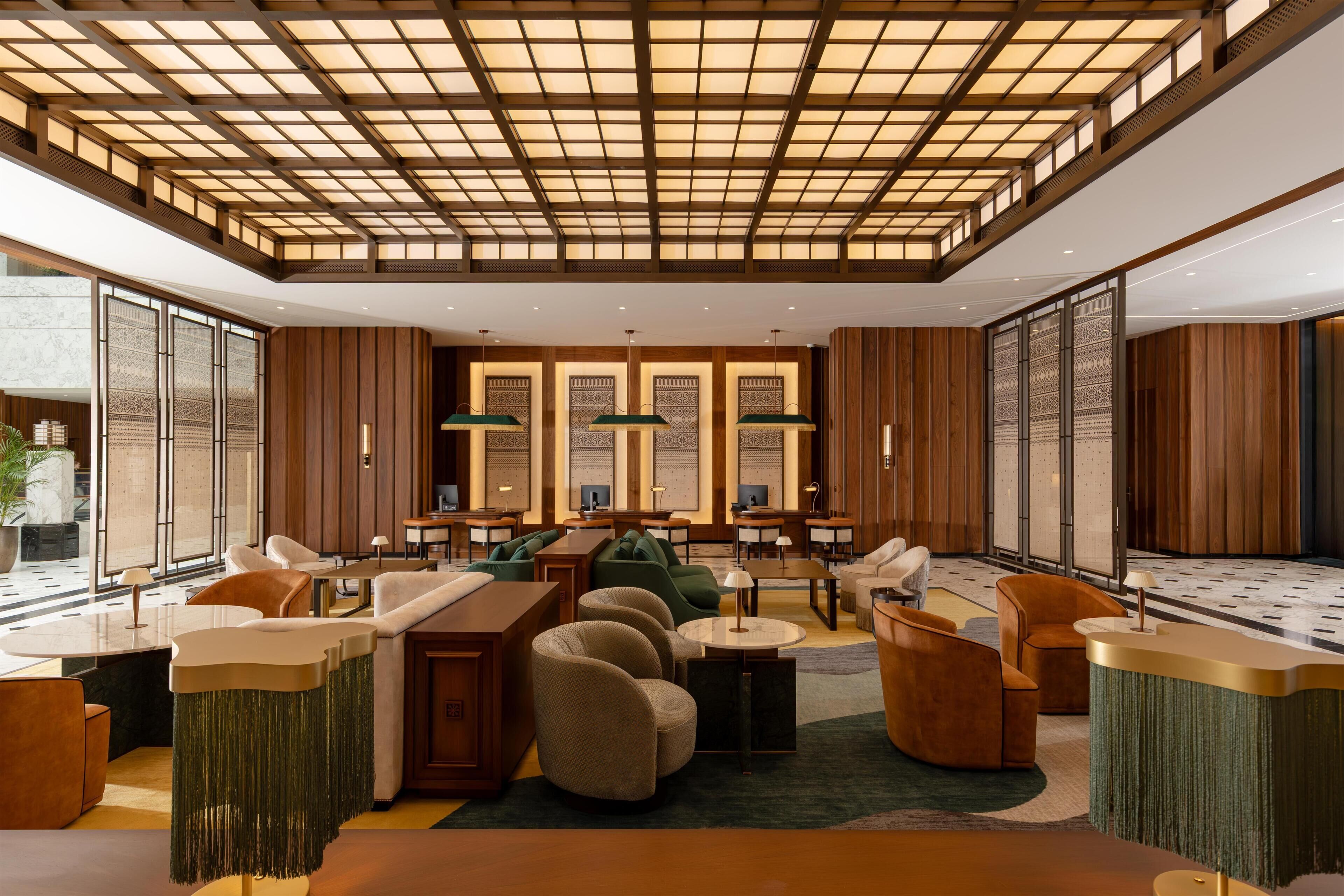 A spacious lobby with a high ceiling, wooden paneling, and a central seating area with tables and chairs.