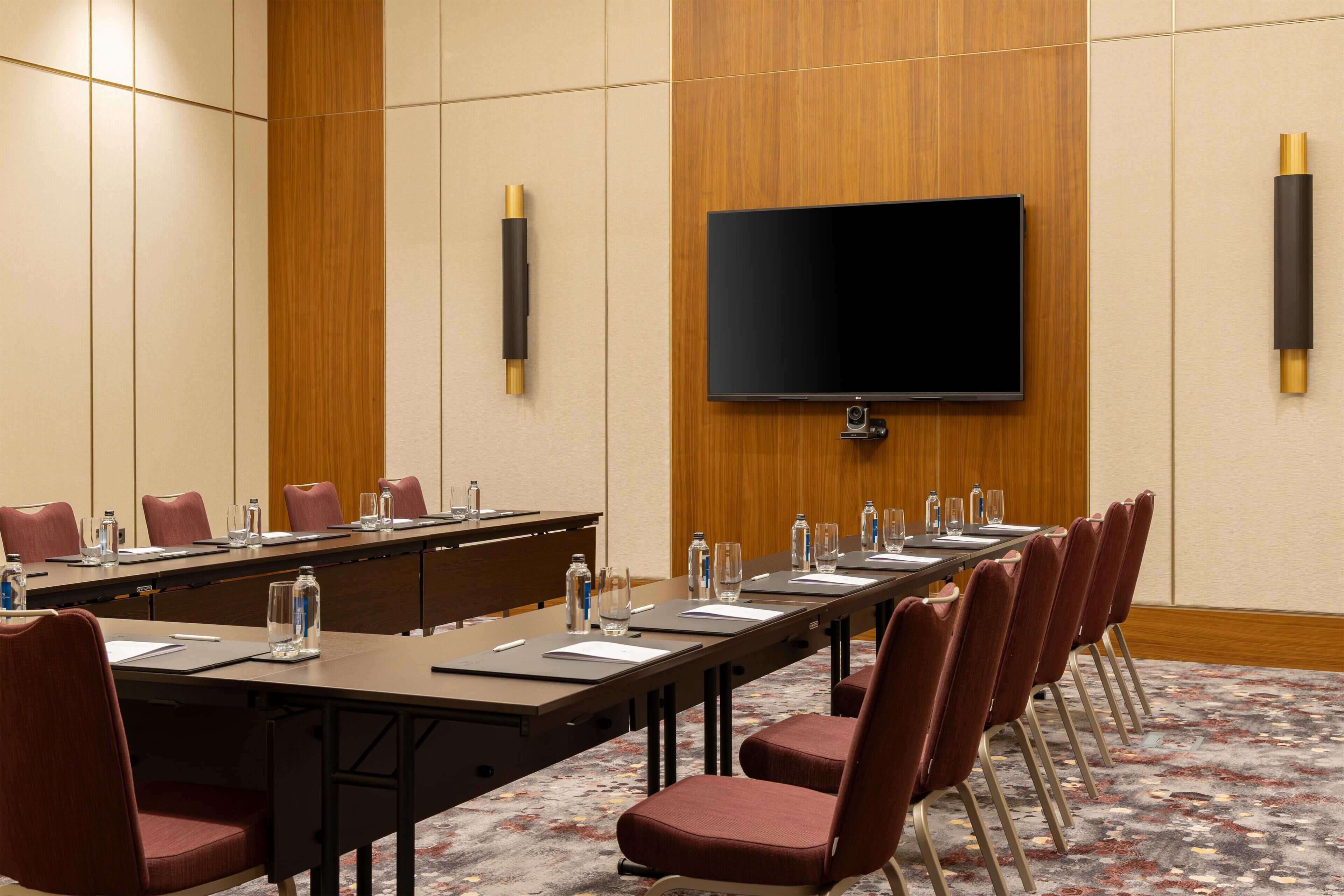 A conference room with a long table, chairs, a flat-screen TV, and a carpeted floor.