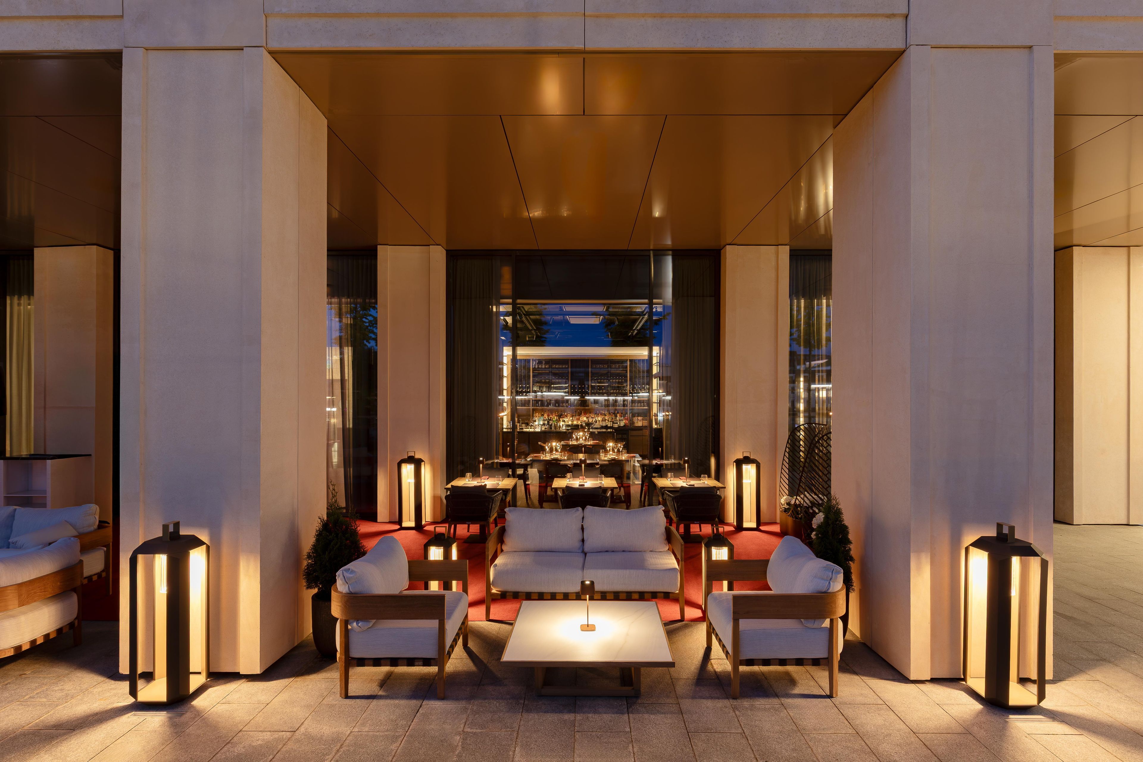 An outdoor seating area with tables and chairs, a bar in the background, and a modern architectural design.