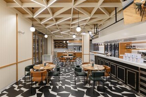 Ein modernes Restaurant mit einem geometrisch gemusterten Boden, Holzbalkendecke und Pendelleuchten.