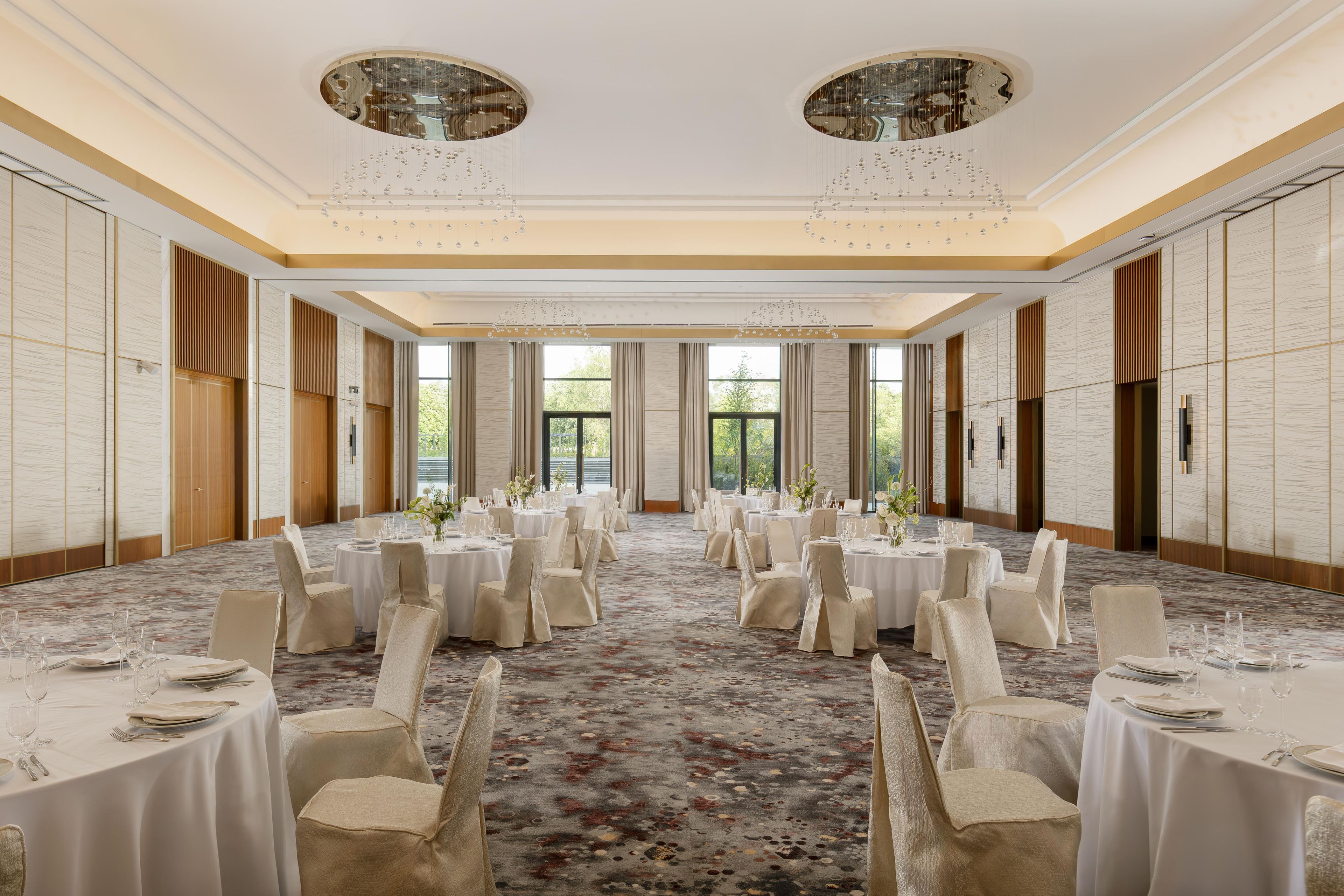 Un amplio salón de banquetes con mesas redondas, sillas y piso alfombrado.