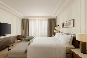 Ein Hotelzimmer mit einem großen Bett, einem Fernseher, einem Schreibtisch und einem Sessel.