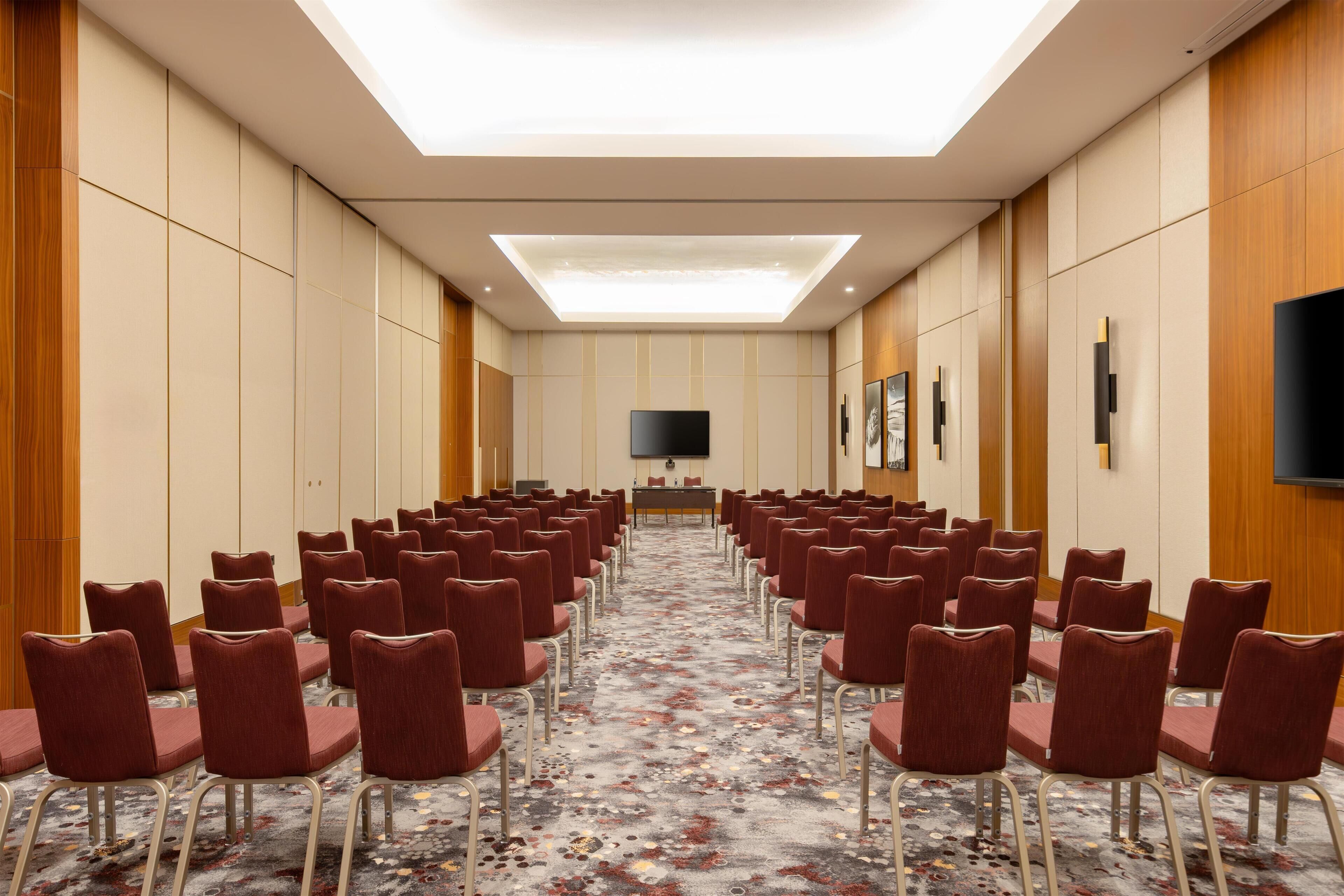A conference room with rows of chairs, a flat-screen TV, and a patterned carpet.