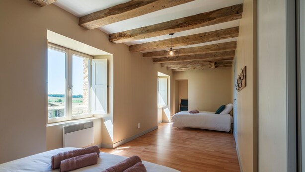 Ein Schlafzimmer mit großem Fenster, Holzbalken, einem Bett mit aufgerollten Handtüchern und Blick ins Freie.