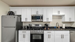 Una cocina moderna con armarios blancos, un refrigerador de acero inoxidable, un microondas, una estufa y un horno.