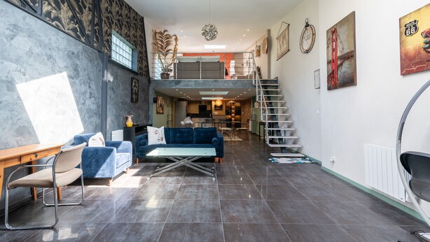 A spacious living area with a high ceiling, a staircase, and a dining area.