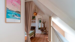 A narrow hallway with wooden flooring, a bed with a green bedspread, a hanging lamp, and a framed poster on the wall. - Le petit Cocon d'Auray - Duplex, proche port St goustan (Auray)
