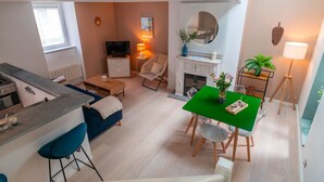 A compact living space with a kitchenette, a dining area, a sofa, a TV, a fireplace, and a small table with a green top. - Le petit Cocon d'Auray - Duplex, proche port St goustan (Auray)