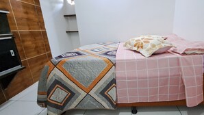 A bedroom with a bed covered in patterned bedding, a bedside table, and a wall-mounted shelf. - Apartamento 2 Praia Morro de São Paulo  (Cairu)