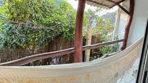 A hammock under a wooden pergola with a view of a lush garden and a bamboo fence. - Apartamento 2 Praia Morro de São Paulo  (Cairu)