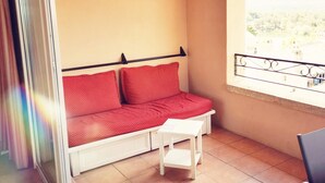 A small balcony with a red sofa and a white table, a window with a metal railing, and a view of a distant landscape. - A little cocoon in Provence on the Pont Royal golf course (Mallemort)