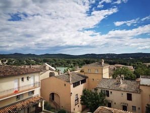 A view of a town with terracotta-roofed buildings, a river in the background, and a clear sky.