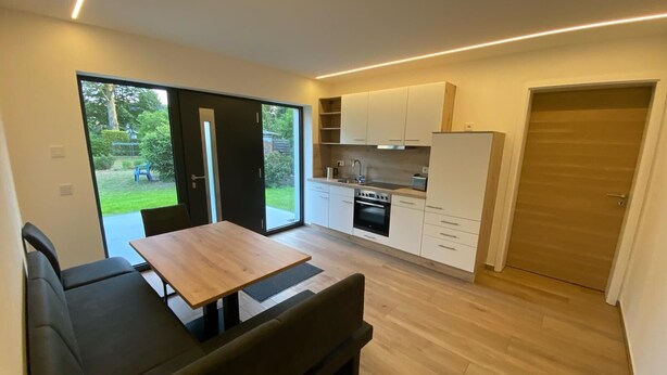 A modern kitchen with white cabinets, a built-in oven, and a dining area with a bench and table. - Renovated vacation home in a quiet location on the outskirts of Berlin (Falkensee)