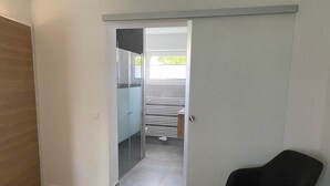 A modern room with a wooden floor, a black chair, and a sliding door leading to a balcony with a white railing. - Renovated vacation home in a quiet location on the outskirts of Berlin (Falkensee)