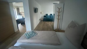 A hotel room with a bed, a wooden coat rack, a TV mounted on the wall, and a view into the adjacent living area. - Renovated vacation home in a quiet location on the outskirts of Berlin (Falkensee)