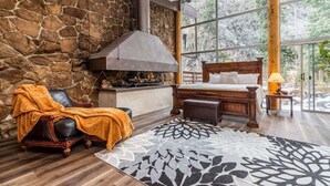 Une chambre avec un mur en pierre, une cheminée, un lit et une grande fenêtre.
