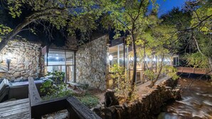 Un bâtiment en pierre avec des fenêtres en verre, une terrasse en bois et un ruisseau.