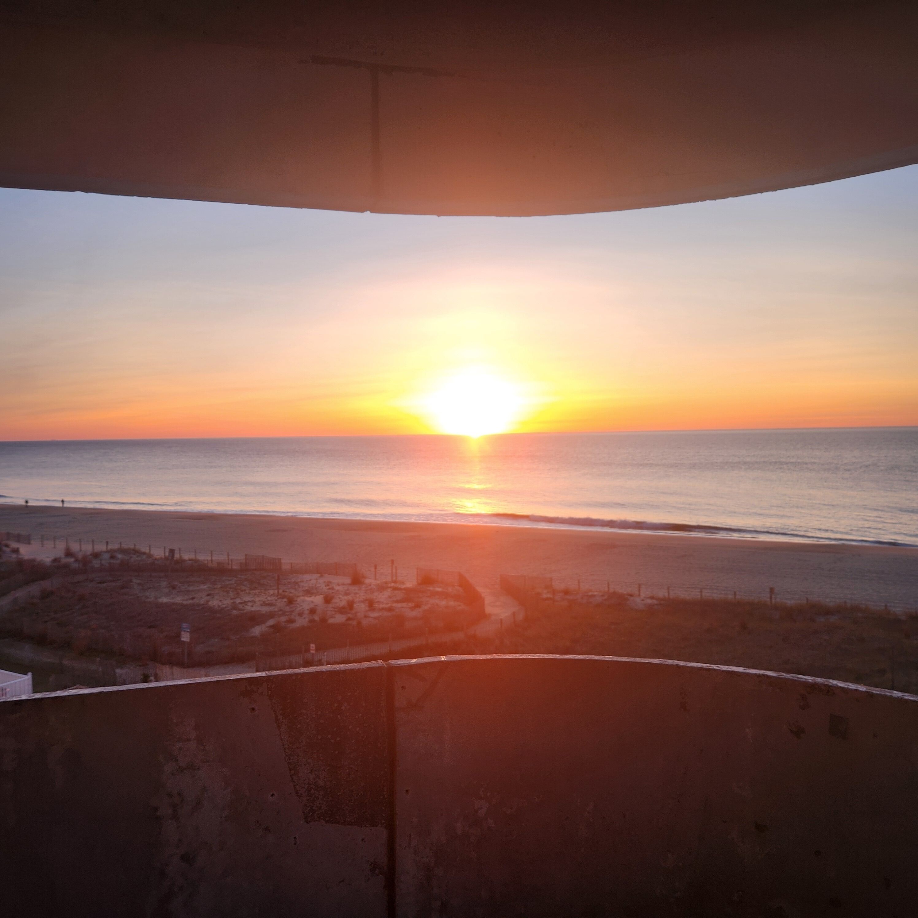 Un tramonto su una spiaggia con una recinzione in primo piano.