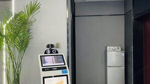 A self-service kiosk, a refrigerator, and a potted plant in a room with a tiled floor and a plain wall. - Urumqi Sundan Yakaifu Theme Hotel (Urumqi)