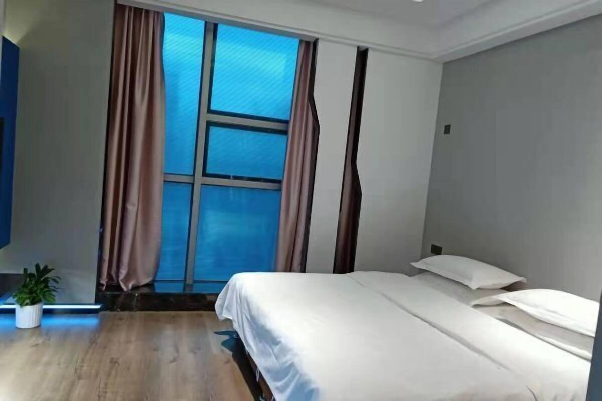 Een hotelkamer met een groot raam, een bed, een kleine potplant en een flatscreen-televisie.