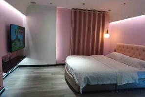 A bedroom with a bed, a television, and a wall-mounted light fixture.