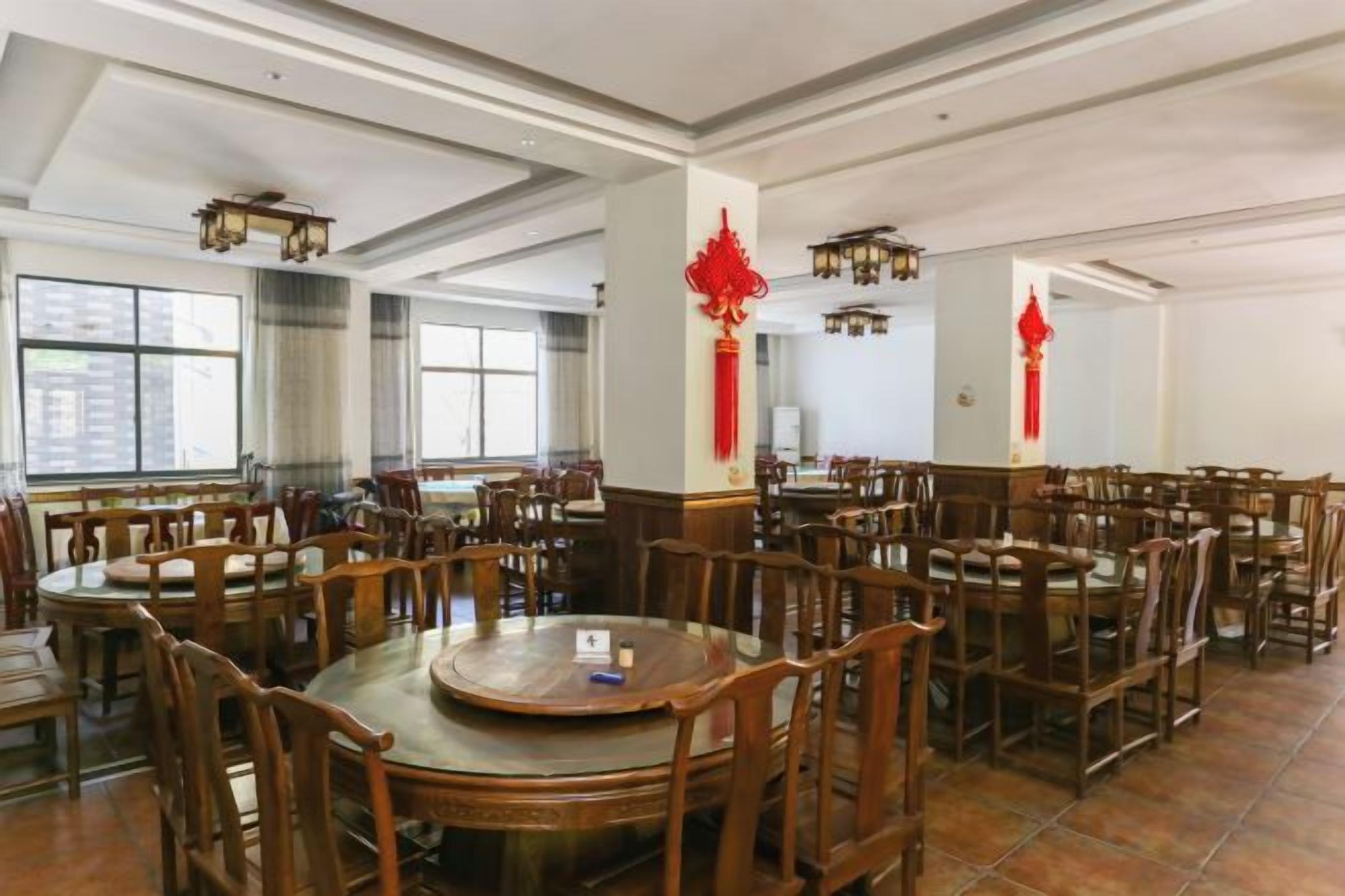 A spacious dining hall with multiple round tables and chairs, large windows, and traditional red decorations.