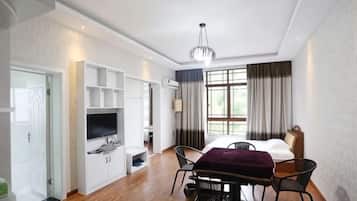 A hotel room with a bed, a TV, a dining table with chairs, a window with curtains, and built-in shelves.