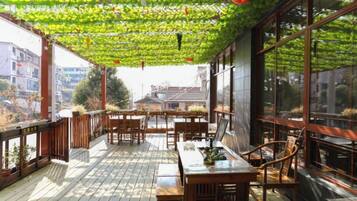A covered outdoor seating area with wooden furniture and large windows.