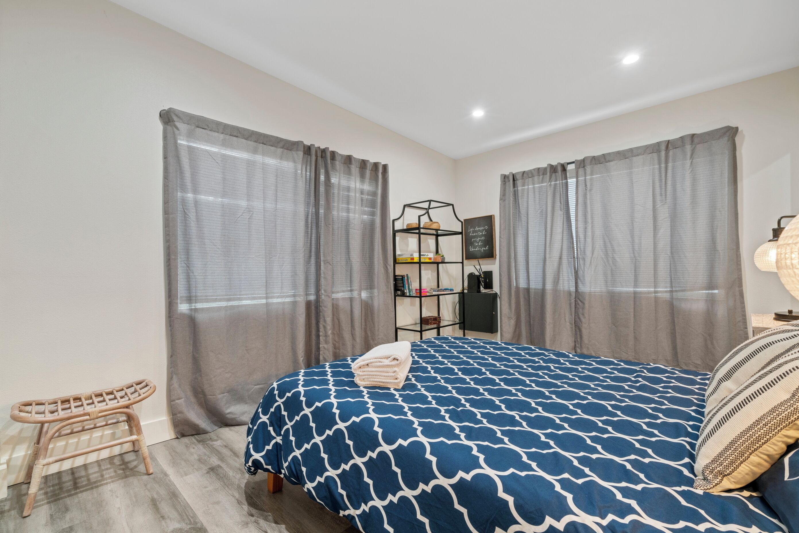 Una camera da letto con un letto, tende, uno scaffale con libri e una piccola sedia.