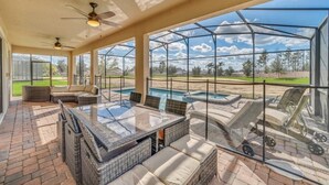 A sunlit patio with a glass-enclosed pool, outdoor furniture, and a view of the surrounding landscape.