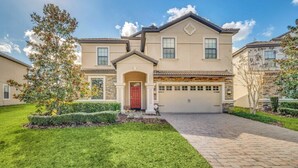 A two-story house with a red door, a garage, and a well-maintained lawn.