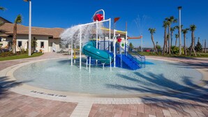 A water play area with a blue slide and a red ball pit, surrounded by palm trees and a clear blue sky.
