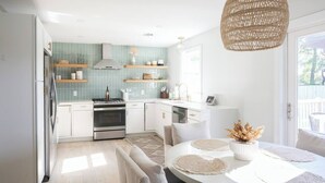 A modern kitchen with white cabinets, a stove, and a dining area with a round table and chairs. - Charleston House with Private Pickleball Court! (Charleston)